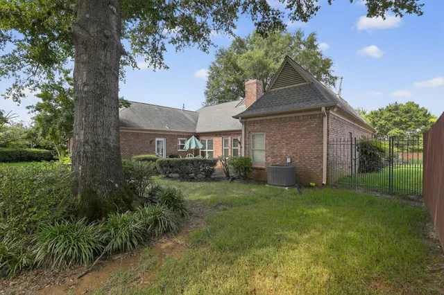 a view of a brick house next to a yard with big trees