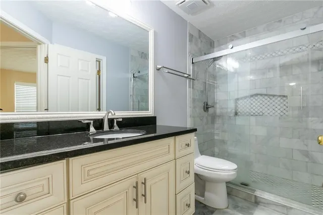 a bathroom with a granite countertop sink a toilet a mirror and shower