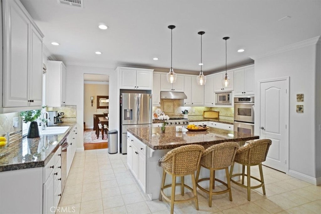 26511 Brooks Circle Stevenson Ranch, CA 91381 - Photo 13 of 55 a kitchen with stainless steel appliances kitchen island granite countertop a refrigerator a stove a sink a dining table and chairs with wooden floor
