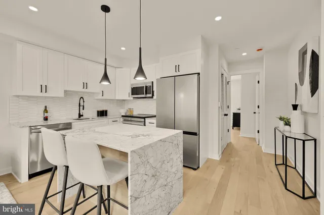 a kitchen with stainless steel appliances kitchen island granite countertop a refrigerator a stove and white cabinets with wooden floor