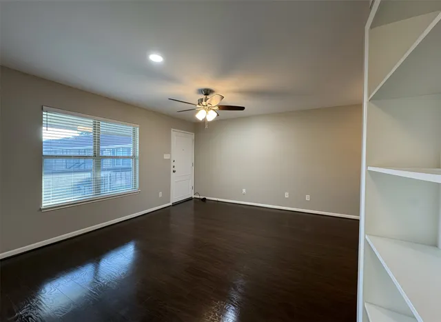 an empty room with wooden floor chandelier fan and windows