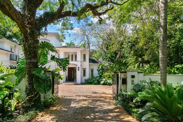 a view of a white house next to a road with large trees