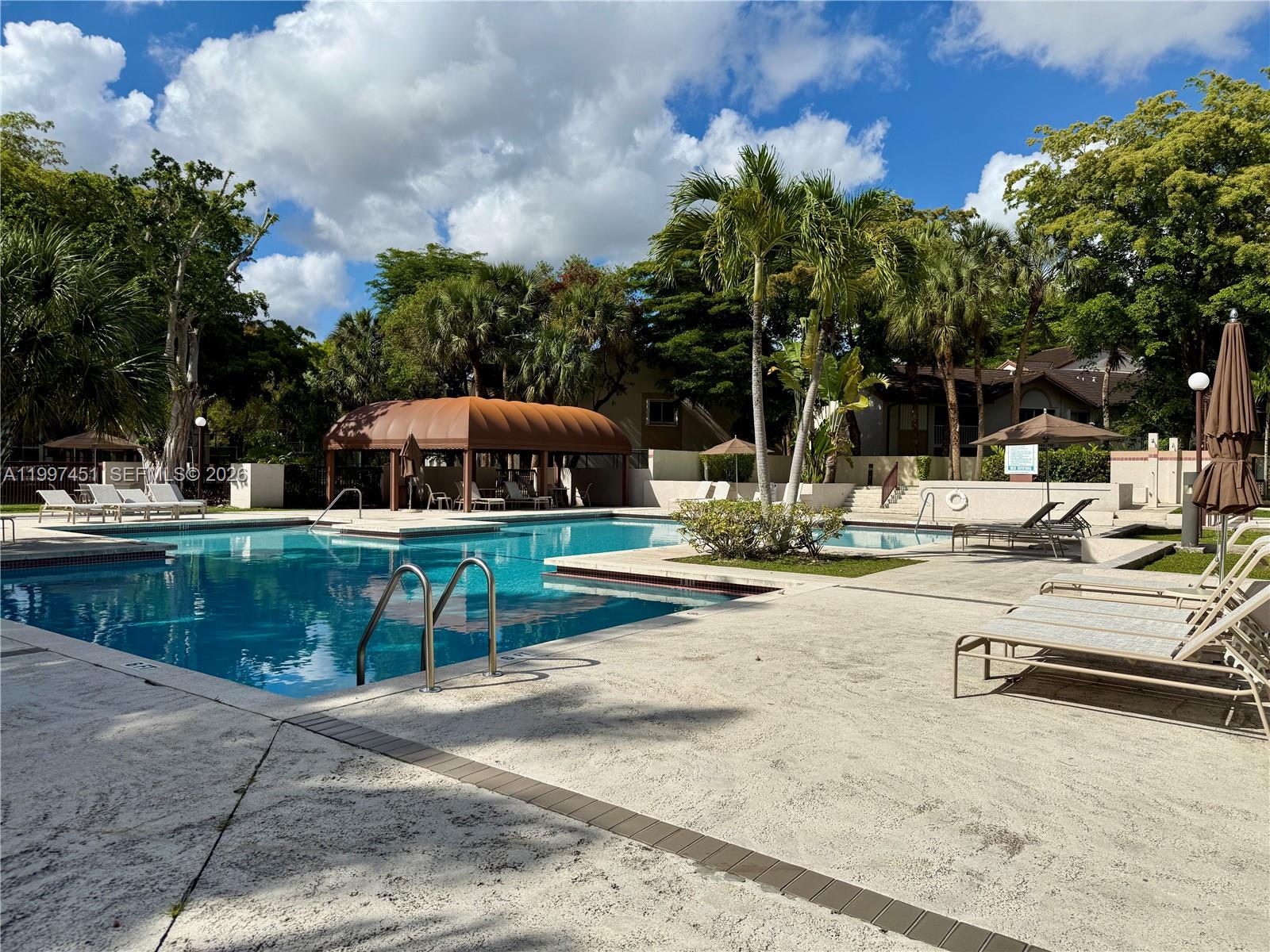 9435 Southwest 140th Court, Unit 9435 Miami, FL 33186 - Photo 2 of 33 a view of a swimming pool with lawn chairs under an umbrella