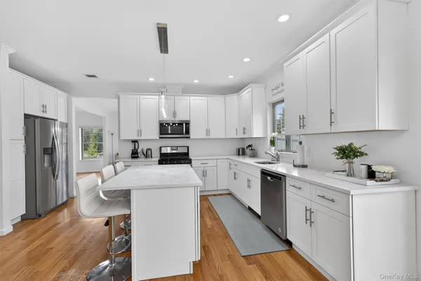 a kitchen with stainless steel appliances granite countertop a refrigerator a stove a sink and white cabinets with wooden floor
