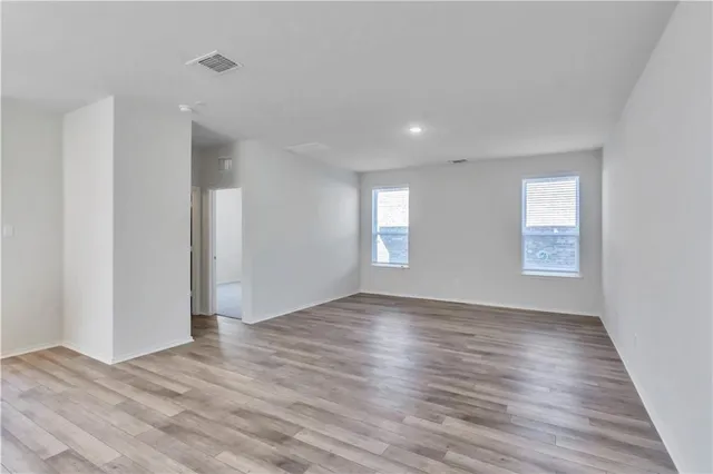 a view of an empty room with wooden floor and window