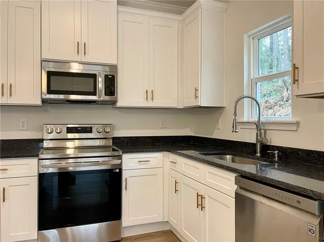 a kitchen with stainless steel appliances granite countertop white cabinets a sink and a stove
