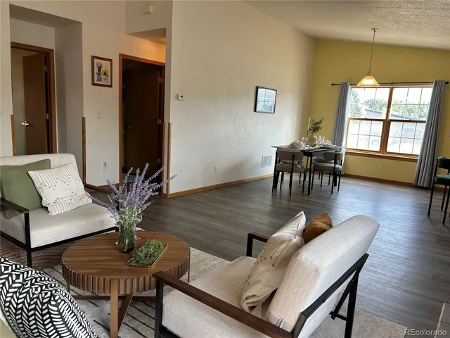 a living room with furniture kitchen area and a wooden floor