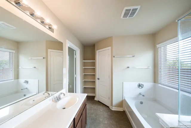 a bathroom with a tub 2 sink and a large mirror