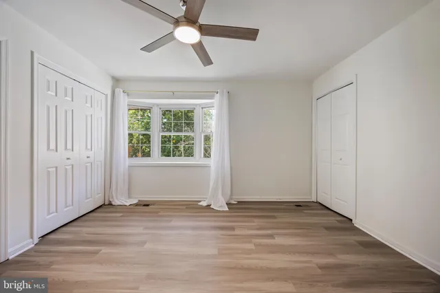 an empty room with wooden floor chandelier fan and windows