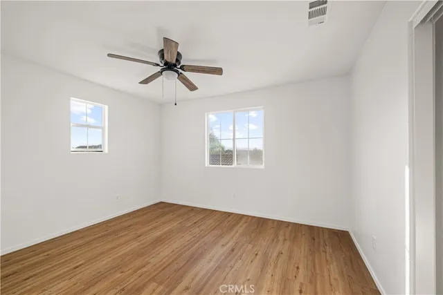 an empty room with wooden floor fan and windows