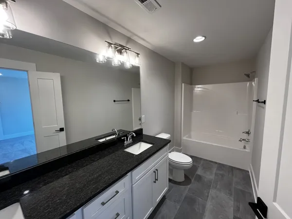 a bathroom with a granite countertop sink a toilet a mirror and shower