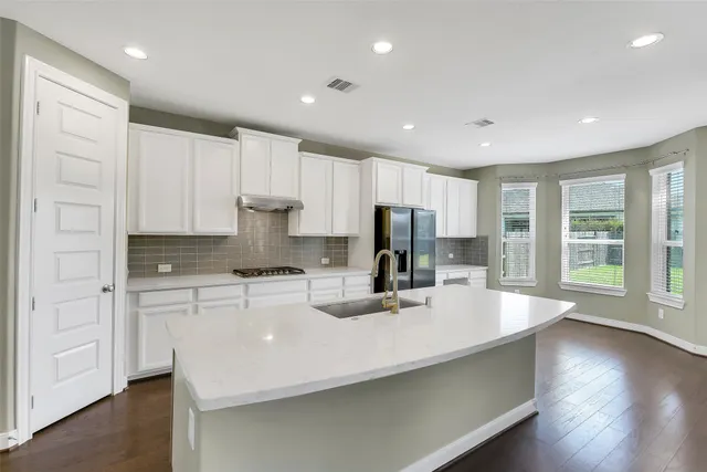 a large white kitchen with sink a refrigerator and wooden floor