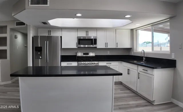 a kitchen with stainless steel appliances granite countertop a sink a stove a refrigerator a counter space and a window