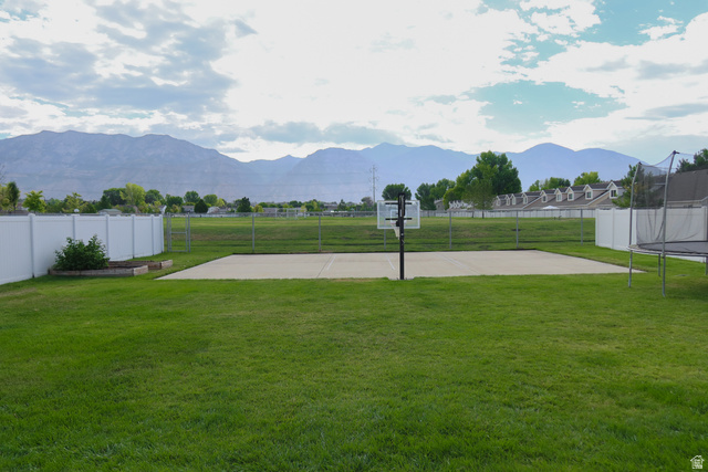 1204 North 3020th Street West Provo, UT 84601 - Photo 6 of 35 Backyard featuring a concrete sports court with an adjustable basketball hoop, a large grassy area, white vinyl perimeter fencing, and garden beds