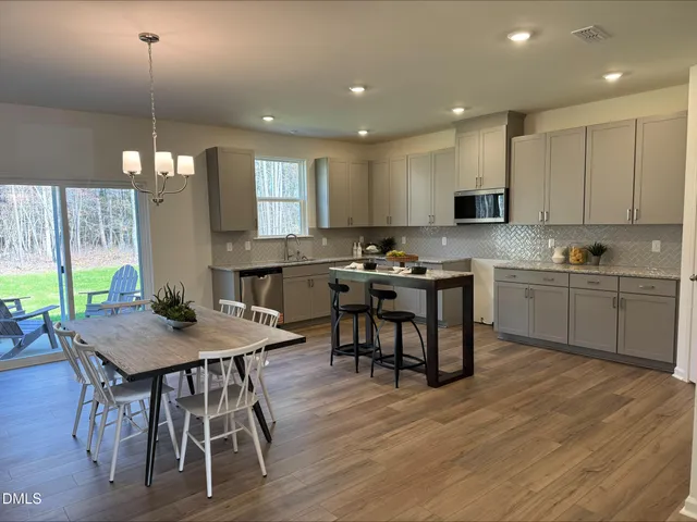 a kitchen with stainless steel appliances granite countertop a stove a sink a microwave a dining table and chairs with wooden floor