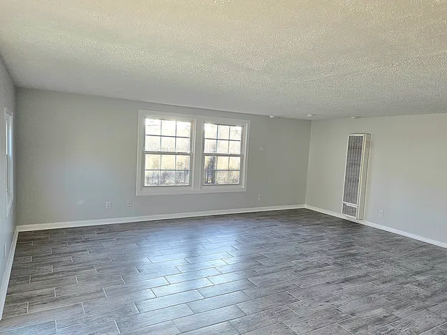 a view of an empty room with wooden floor and window