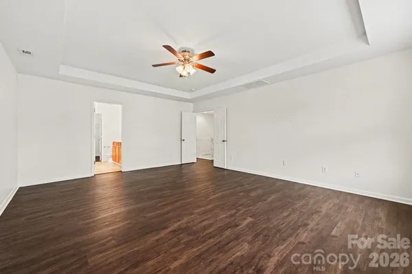 a view of an empty room with wooden floor and a ceiling fan