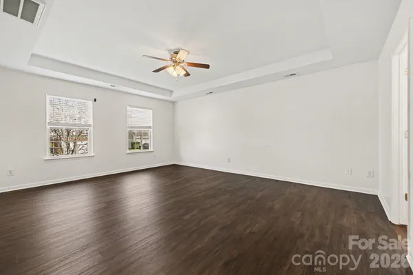 an empty room with wooden floor chandelier fan and windows