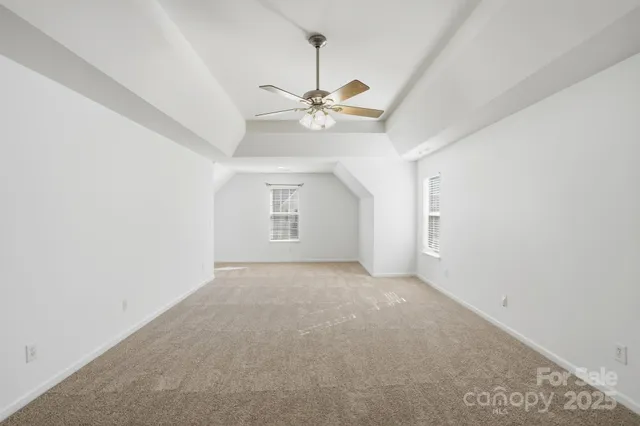 an empty room with chandelier fan and windows