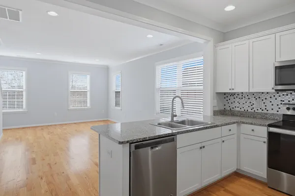 a kitchen with granite countertop a sink dishwasher a stove and white cabinets with wooden floor