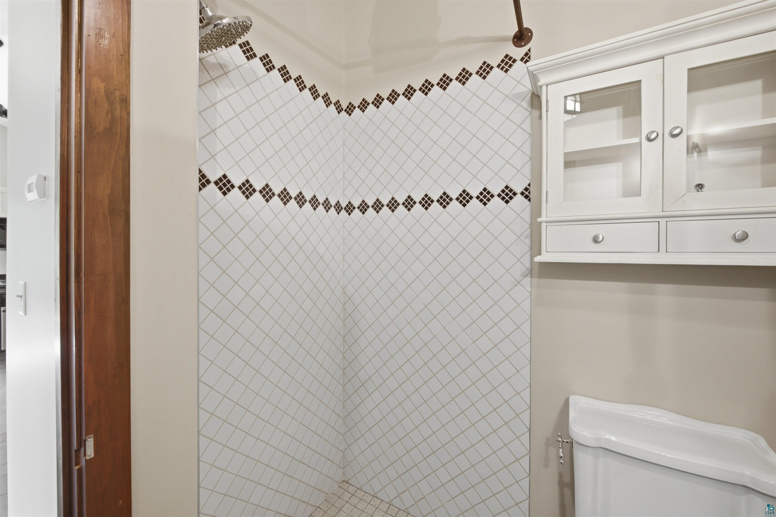 86270 Meyers-Olson Road Bayfield, WI 54814 - Photo 19 of 33 Shower stall featuring white diagonal tile with decorative brown accents, a rain showerhead, and a bronze-finish shower rod