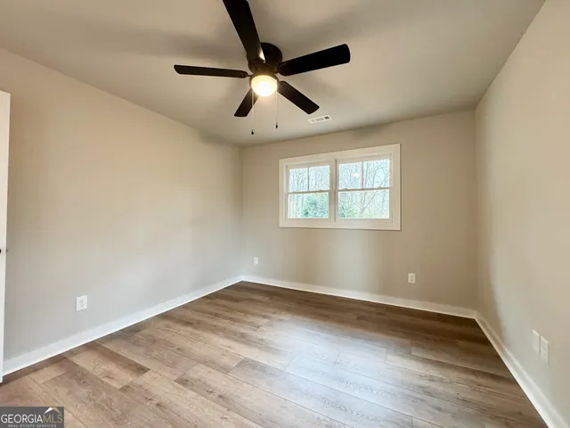 an empty room with wooden floor ceiling fan and windows