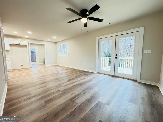 a view of an empty room with wooden floor and a ceiling fan