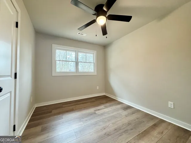 an empty room with wooden floor fan and windows