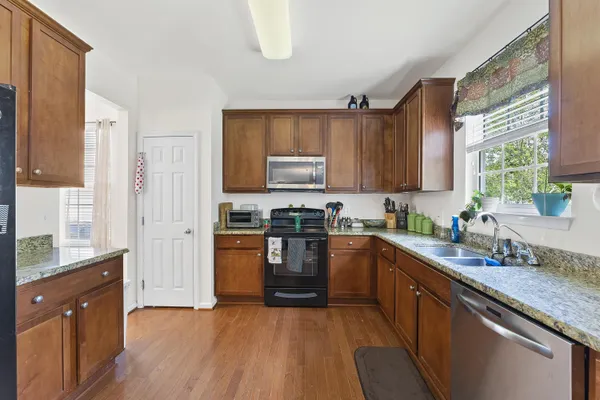 a kitchen with stainless steel appliances granite countertop wooden cabinets a sink a stove a refrigerator and dishwasher with wooden floor