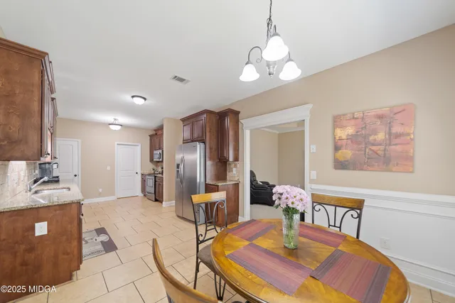 a kitchen with stainless steel appliances kitchen island granite countertop a refrigerator a sink a dining table and chairs with wooden floor