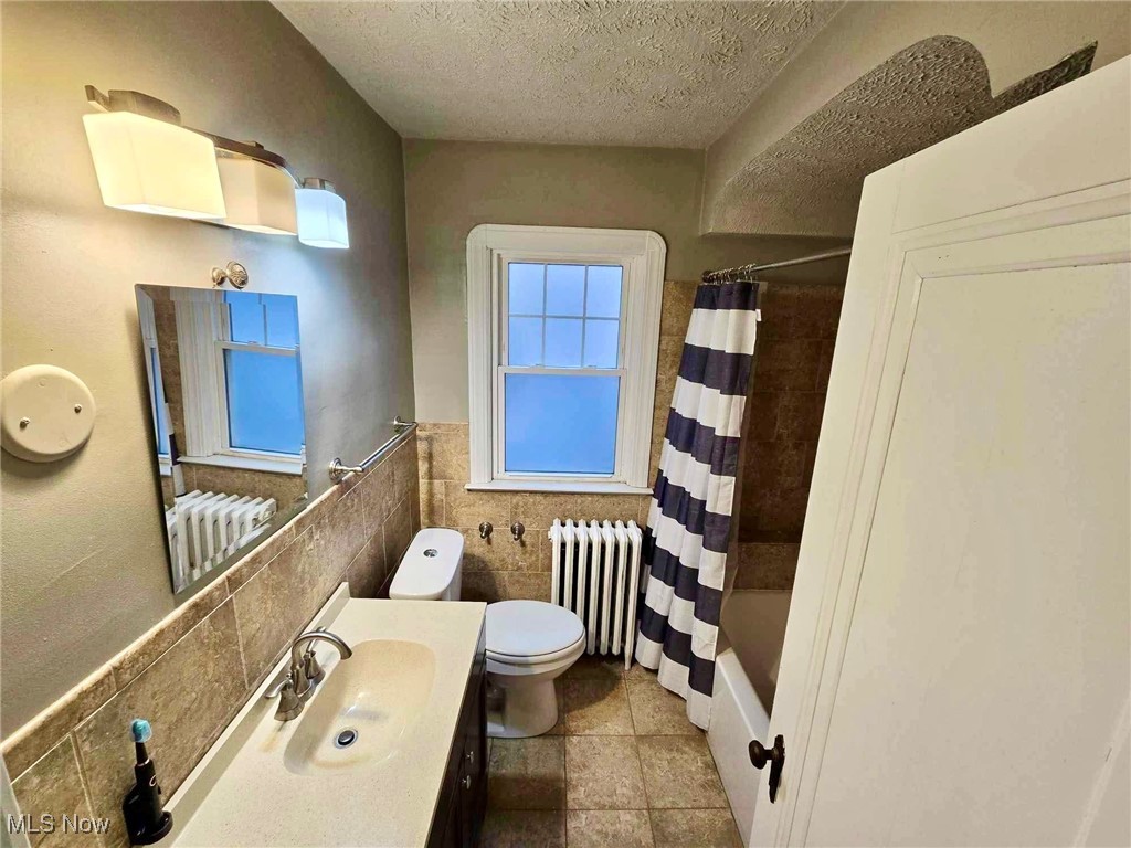 3505 Silsby Road Cleveland, OH 44118 - Photo 16 of 34 Full bathroom with a textured ceiling, shower / bathtub combination with curtain, tile walls, radiator heating unit, and toilet