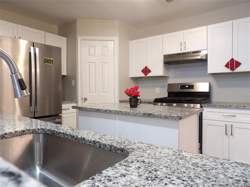223 Juniper Ridge Court DeSoto, TX 75115 - Photo 7 of 33 Kitchen with stainless steel appliances, white cabinetry, light stone countertops, and a center island