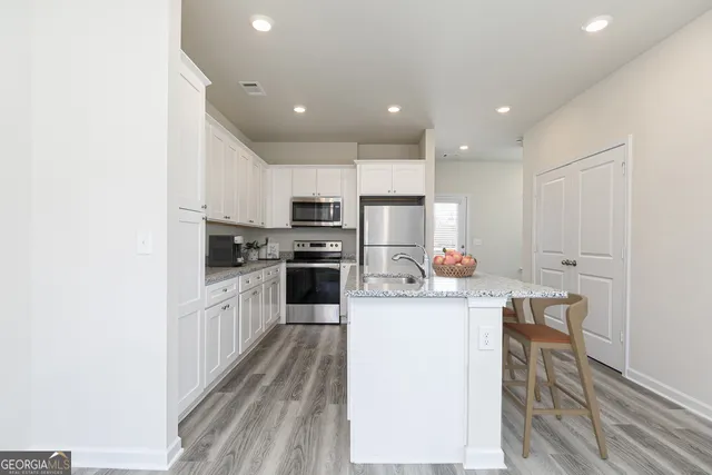 a kitchen with stainless steel appliances a microwave a stove a sink dishwasher and white cabinets with wooden floor