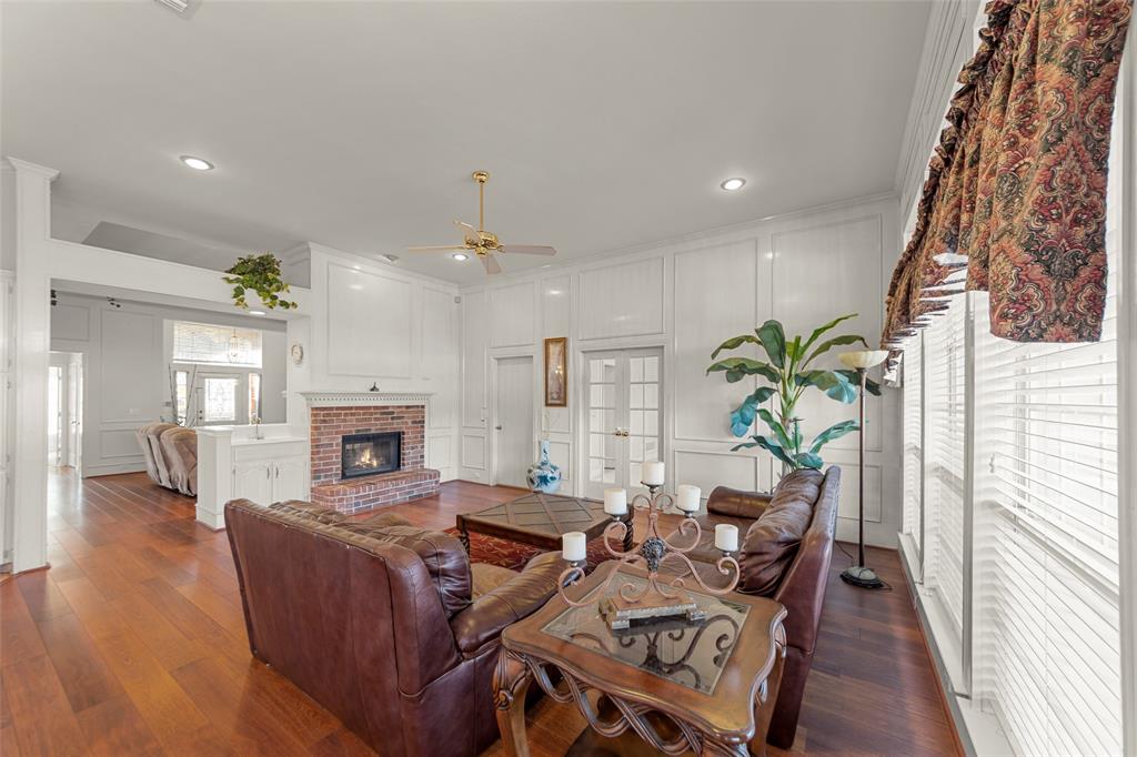 3308 North Spring Drive Richardson, TX 75082 - Photo 6 of 38 The family room showcases soaring ceilings and elegant paneled walls that create a grand yet inviting atmosphere. Rich wood-like flooring adds warmth and durability, flowing seamlessly throughout the space. A charming brick fireplace serves as a cozy focal point, while large windows fill the room with abundant natural light. Spacious yet comfortable, this inviting area is perfect for both everyday living and entertaining.