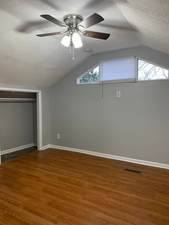 an empty room with wooden floor fan and windows