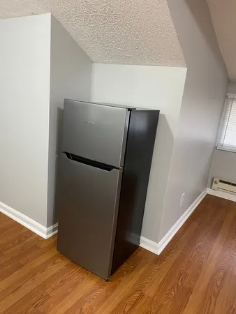 a view of a refrigerator in kitchen and an empty room with wooden floor