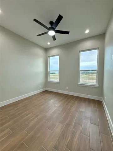an empty room with wooden floor fan and windows