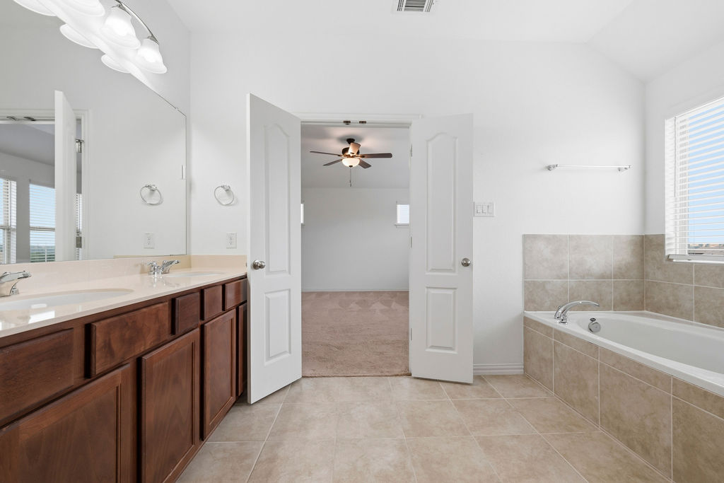 1005 Ridge Runner Drive Georgetown, TX 78628 - Photo 21 of 32 Bathroom featuring a dual vanity with a light-toned countertop, a built-in soaking tub with tile surround, and neutral tile flooring