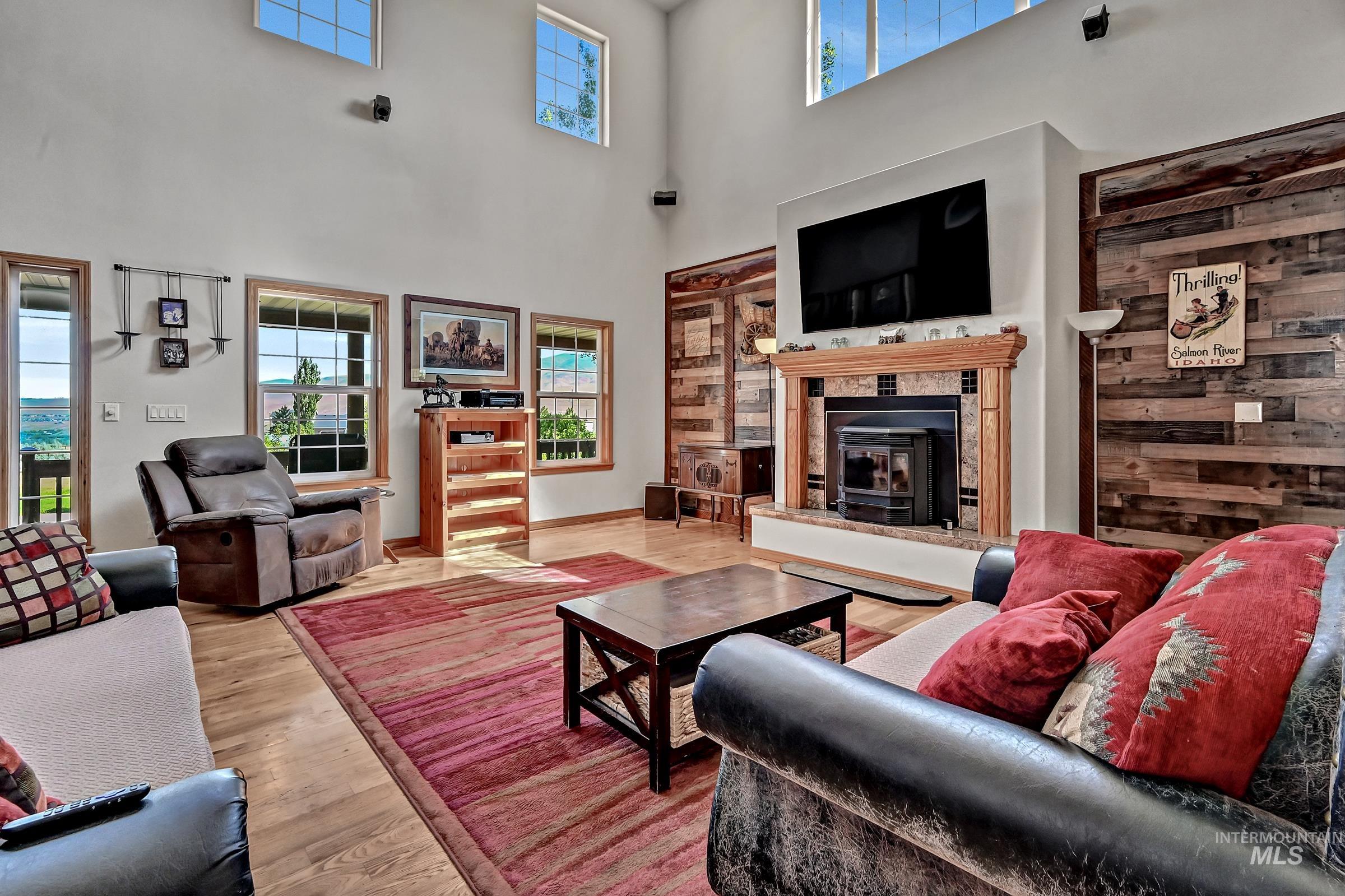 7213 East Columbia Road Boise, ID 83716 - Photo 7 of 47 Vaulted ceilings with upper windows, wood-finish flooring, a wood-burning stove with a tile surround and wood mantel, and accent walls featuring horizontal wood paneling