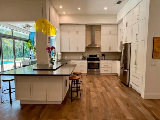 a kitchen with stainless steel appliances a stove a refrigerator a sink and white cabinets with wooden floor