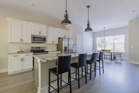 a kitchen with stainless steel appliances granite countertop a stove a sink a microwave a dining table and chairs with wooden floor