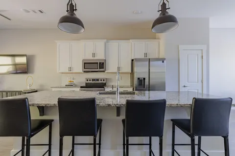 a kitchen with stainless steel appliances kitchen island granite countertop a dining table chairs and a refrigerator