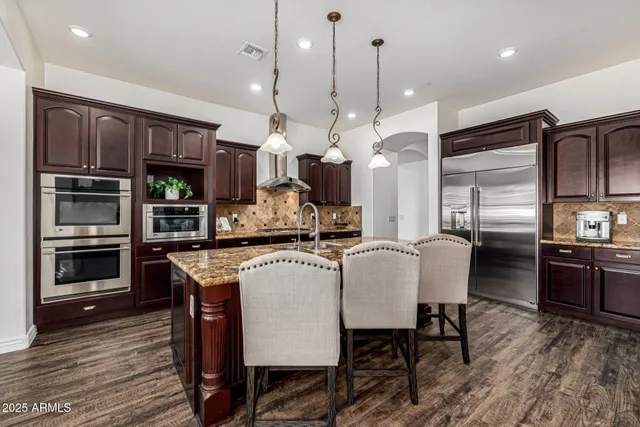 a kitchen with stainless steel appliances granite countertop a stove a refrigerator a oven a sink a dining table and chairs with wooden floor