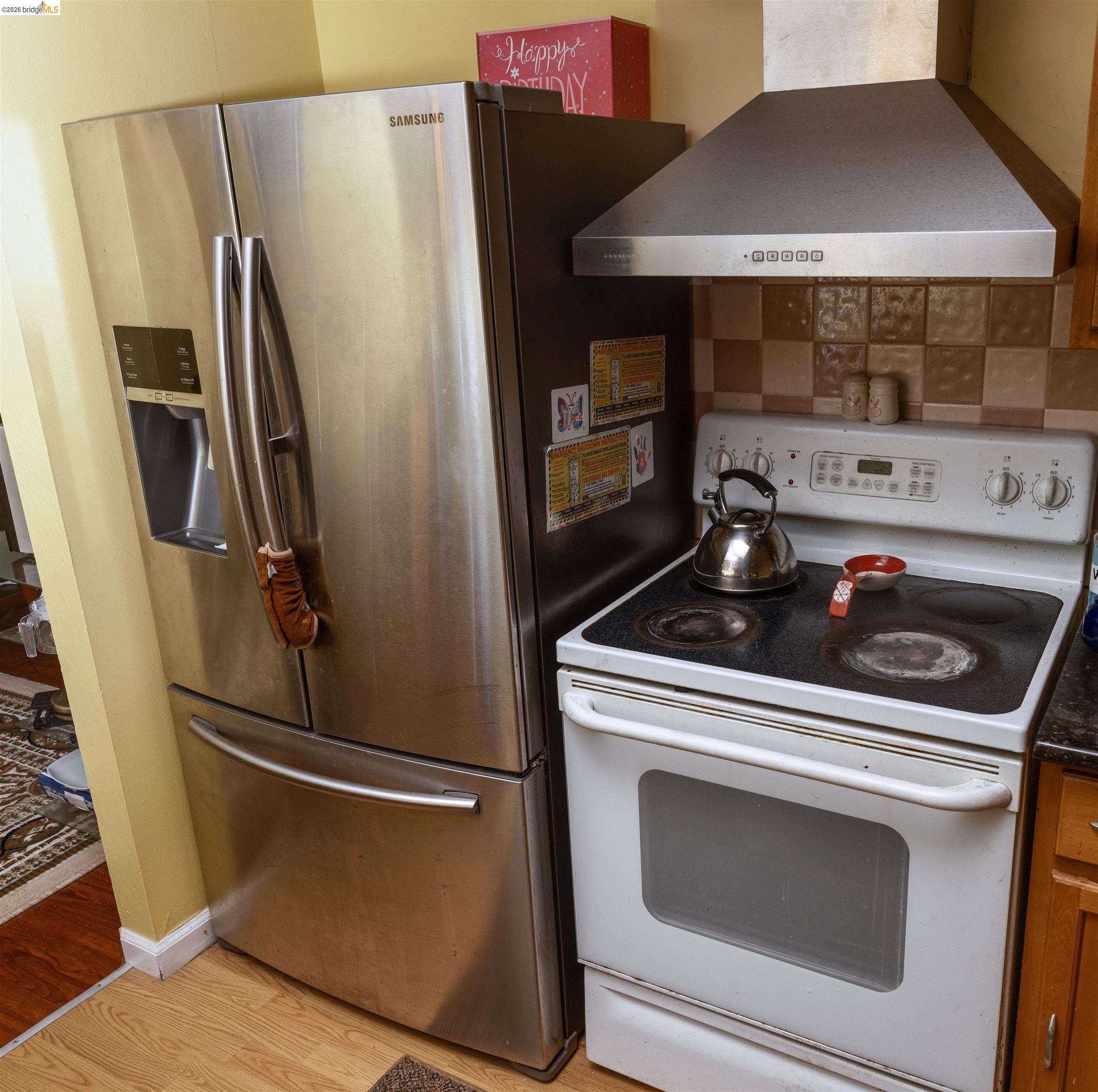 767 Marlesta Road Pinole, CA 94564 - Photo 6 of 16 Stainless steel French door refrigerator with ice and water dispenser, accompanied by a white electric range and a stainless steel range hood