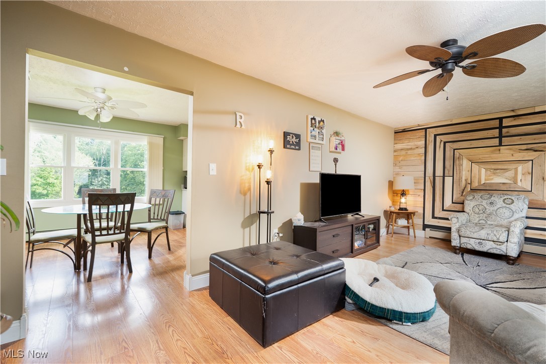 Living room with ceiling fan, baseboard heating, and light hardwood / wood-style flooring