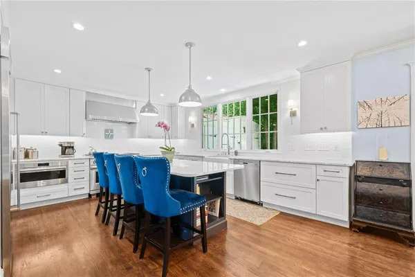 a kitchen with stainless steel appliances kitchen island granite countertop a stove a sink a dining table and chairs with wooden floor