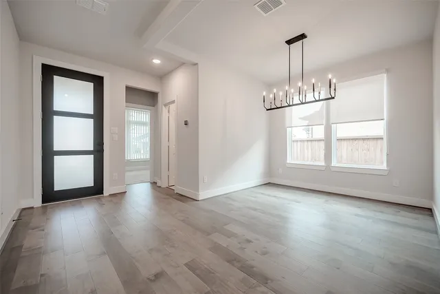 an empty room with wooden floor chandelier and windows