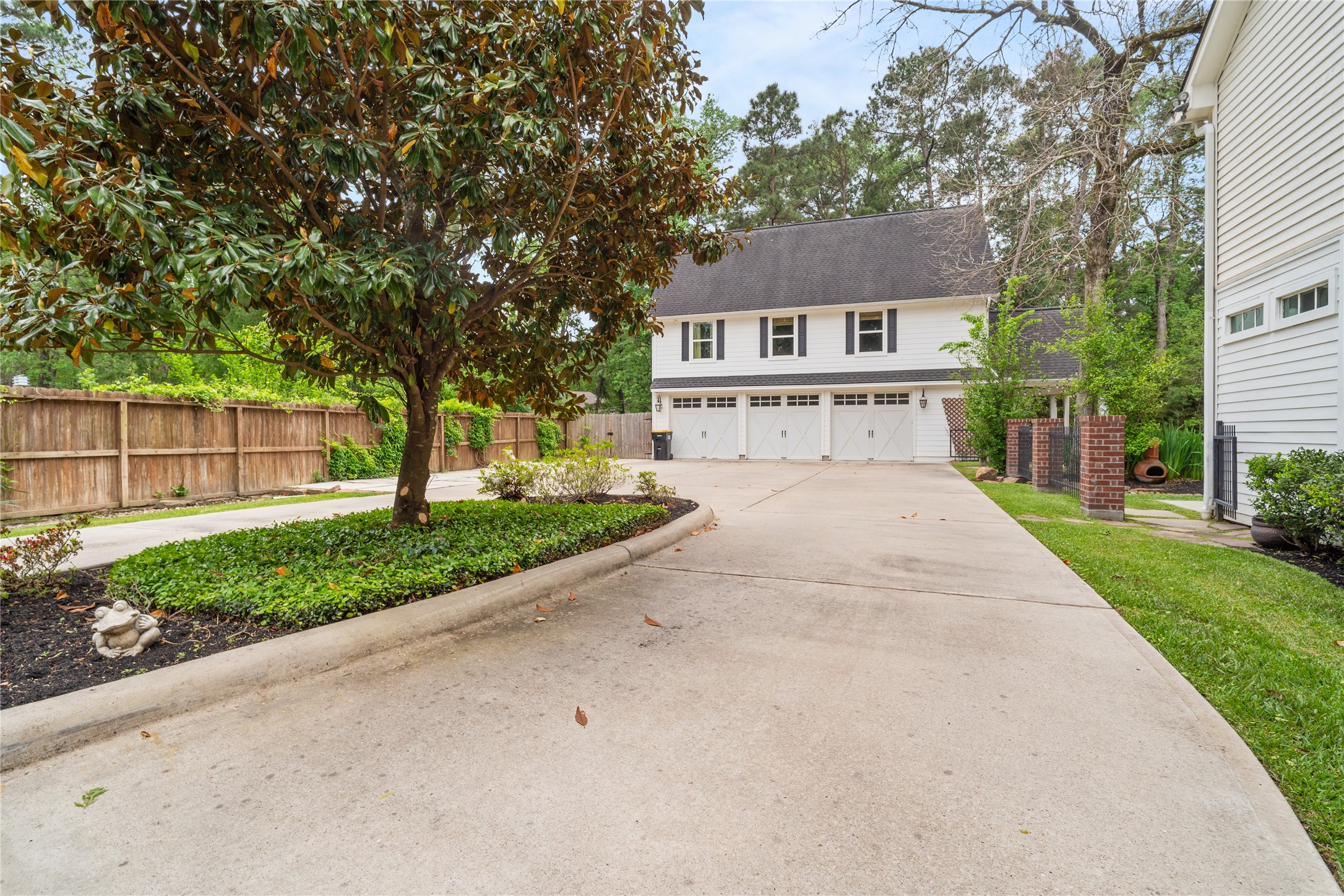 36 Wind River Drive Conroe, TX 77384 - Photo 8 of 45 This photo showcases a spacious driveway leading to a multi-car garage, surrounded by a well-maintained lawn and mature trees. The house features a classic exterior with white siding and a large roof. The area is fenced, providing privacy and a serene, wooded backdrop.