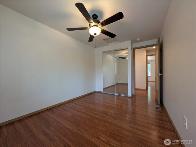 a view of an empty room with wooden floor and a ceiling fan