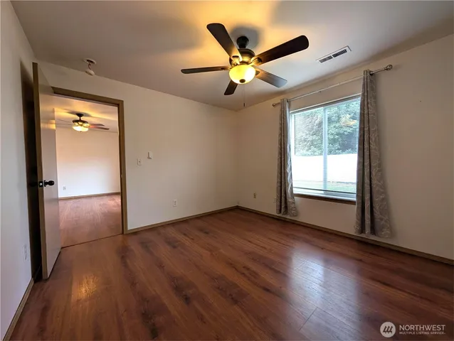 an empty room with wooden floor fan and windows